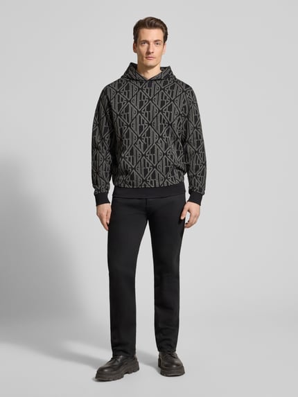 Mannenmodel draagt Hoodie im Allover-Look mit Känguru-Tasche van Guess in zwarte katoen, regular fit, allover-patroon, kangoeroezak, volledige lichaamsvoorzijde.