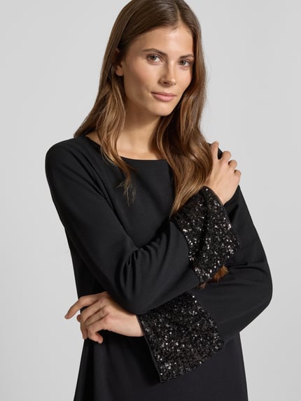 Vrouwenmodel draagt Relaxed Fit Mini-jurk met pailletten van s.Oliver BLACK LABEL, effen look, boothals, lange mouw, zonder sluiting, minilengte. Nahaufnahme bovenlichaam.