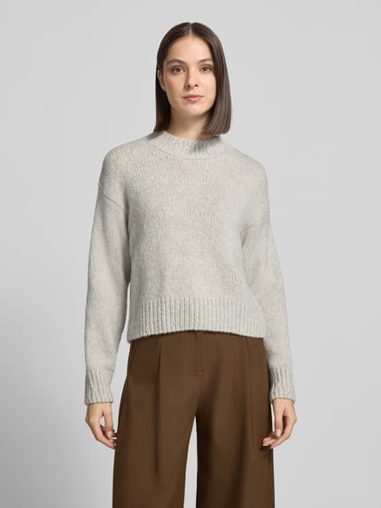 Modelka nosi sweter z alpaki z prążkowanymi ściągaczami od MARC CAIN, krój regular fit, jednokolorowy, imitacja dzianiny, krótki krój, opuszczone ramiona, okrągły dekolt, długi rękaw, prążkowane zakończenia; widok całej sylwetki z przodu.