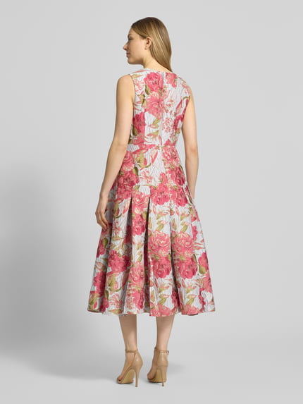 Vrouwenmodel draagt Regular Fit midi-jurk met all-over bloemenmotief-stitching van Adrianna Papell in roze en wit, a-lijn, mouwloos design, ronde hals, elastische materiaalmix, getailleerd, ruglengte maat 36: 115 cm, borstwijdte maat 36: 41 cm, geheelopname achteraan.