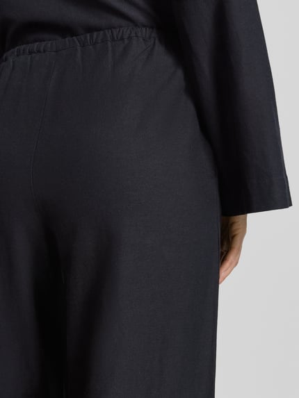 Frauenmodel trägt Stoffhose aus Viskose-Mix Modell 'PRISILLA' von Vila, dunkel, matte Struktur, Eingrifftaschen, Detailaufnahme Rückansicht. Kontext: Damen Stoffhose, Leinen-Viskose-Mix, Wide Leg, Tunnelzug, Bundweite 35 cm, Innenbeinlänge 82 cm bei Größe 36.