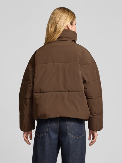 Frauenmodel trägt Steppjacke mit Stehkragen Modell 'Refron' von MSCH Copenhagen in Braun, Material-Mix mit Stretch, Ganzkörperansicht Rückansicht.