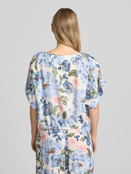Frauenmodel trägt Bluse aus Viskose-Mix mit U-Boot-Ausschnitt von Oui, florales Muster, Gerader-Schnitt, Fledermausärmel, Elastikbündchen, Leinen-Viskose-Anteil, Rückenlänge 48 cm bei Größe 36, Ganzkörperansicht Rückansicht.