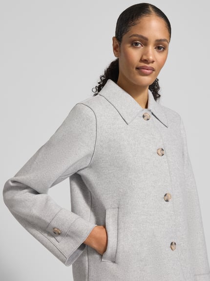 Frauenmodel trägt Jacke mit Umlegekragen Modell 'Juice' von Vila in Hellgrau, Viskose-Materialmix mit Knopfleiste, Eingrifftaschen, Nahaufnahme Oberkörper.