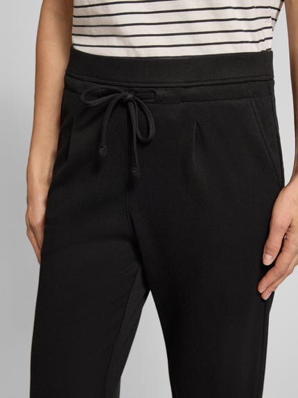 Frauenmodel trägt Hose aus Viskose-Mix mit elastischem Bund und Tunnelzug von Christian Berg Woman, schwarze Farbe, glatte Textur, Nahaufnahme Oberkörper, Regular Fit, sichtbarer Tunnelzug, Kontext: Damen Hose mit Stretch-Anteil, Bundweite 39 cm, Innenbeinlänge 68 cm.