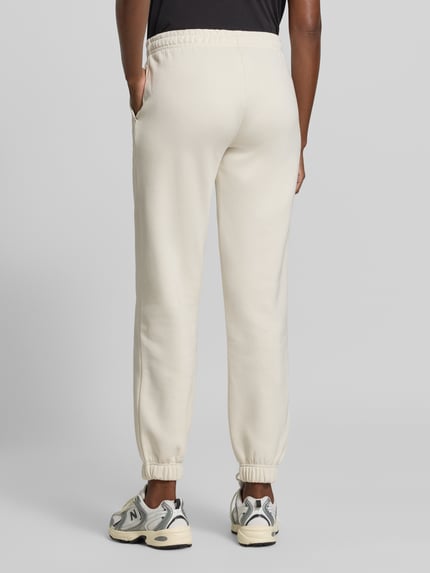 Vrouwenmodel draagt Regular Fit Sweatpants uit katoenmix met labeldetail van aim'n in crème met elastische boordjes, binnenbeenlengte maat S 78 cm, achteraanzicht.