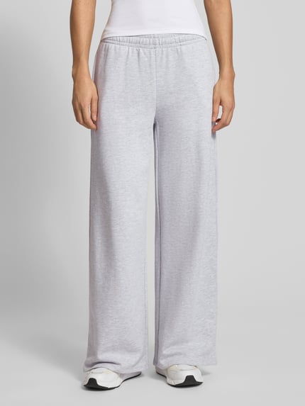 Kobiece model prezentuje Wide Fit Sweatpants mit elastische Bund od Gina Tricot, mieszanka bawełny, krój wide fit, długość wewnętrzna nogawki 76 cm, jasnoszary kolor, struktura gładka, widok z przodu na całe ciało.