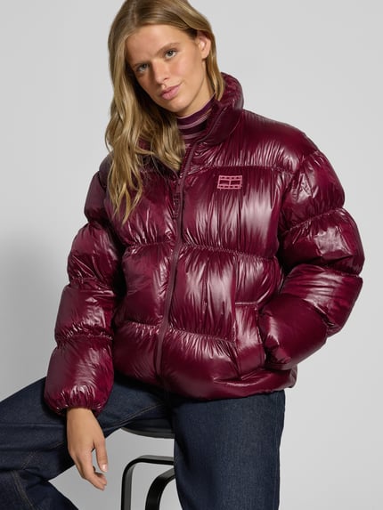 Frauenmodel trägt Regular Fit Steppjacke mit Label Stitching von Tommy Jeans in glänzendem Dunkelrot, unifarben, Nahaufnahme Oberkörper.