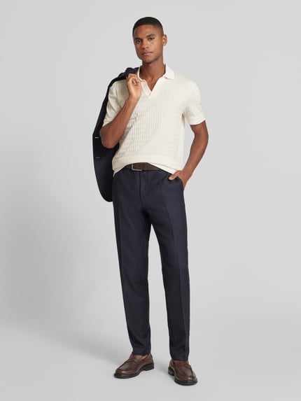 Männermodel trägt Poloshirt mit gerippten Abschlüssen Modell 'Cleison' von JOOP! Collection, reine Baumwolle, Regular-Fit, Polokragen, V-Ausschnitt, dunkle Hose, Ganzkörperansicht von vorne.