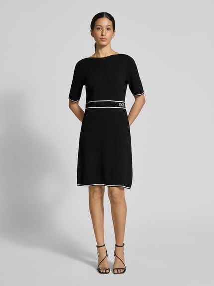 Frauenmodel trägt Regular Fit Kleid aus Viskose-Mix Modell 'Kirla' von JOOP! in Schwarz mit Strick-Optik, Halbarm-Design, Logo-Stitching, Ganzkörperansicht von vorne. Rückenlänge 91 cm, Brustweite 45 cm, Ärmellänge 30 cm.