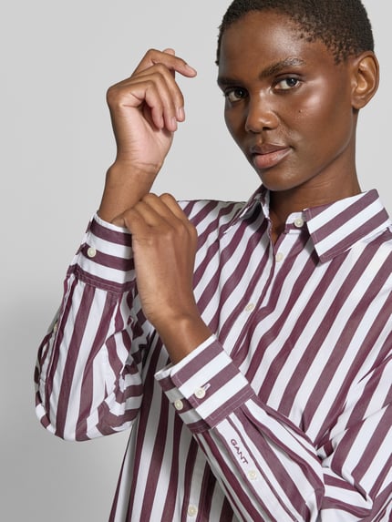 Frauenmodel trägt Relaxed Fit Langarmbluse aus reiner Baumwolle von GANT, gestreift in Weiß und Dunkelrot, Nahaufnahme Oberkörper. Damen Langarmbluse von GANT.