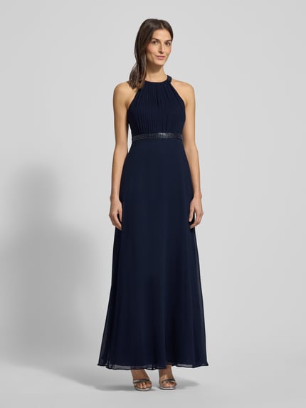 Vrouwenmodel draagt avondkleid met ziersteinbesatz en raffungen van V.M. by Vera Mont, donkerblauw chiffon, unicolor, taillering, maxilengte, neckholder, zichtdichte onderrok, hakenluiting. Ganzkörperansicht van voren.