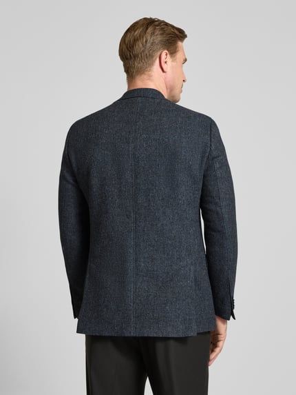 Męski model nosi Slim Fit Sakko mit Viskose-Anteil Modell 'Theo' von Carl Gross, mieszanka materiałów z dodatkiem wiskozy, kolor ciemnoszary melanż, kołnierz z połami, listwa z 2 guzikami, kieszenie z patką, poszetka, długość tyłu w rozmiarze 50: 74 cm, szerokość w rozmiarze 50: 45 cm, długość rękawów w rozmiarze 50: 65 cm, widok całej sylwetki z tyłu.