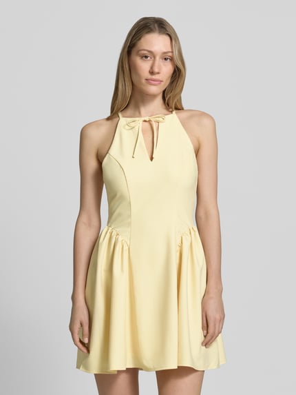 Frauenmodel trägt Cocktailkleid mit Schlüsselloch-Ausschnitt von Little Mistress aus Material-Mix mit Rayon-Anteil, A-Linie, Minikleid, Schnürung, Rückseitiger Reißverschluss, in hellem Gelbton, glatte Textur, Ganzkörperansicht von vorne.