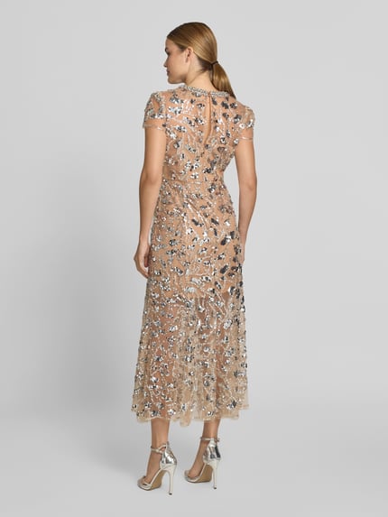 Vrouwenmodel draagt 'Maxikleid mit Allover-Ziersteinbesatz' van Self-Portrait, nude kleur, all-over siersteentjes, getailleerd, semi-transparant, maxi-jurk met korte mouwen, ronde hals, totale lengte maat 36: 136 cm, borstwijdte: 45 cm, mouwlengte: 17 cm, taillewijdte: 37 cm, geheelopname achteraanzicht.