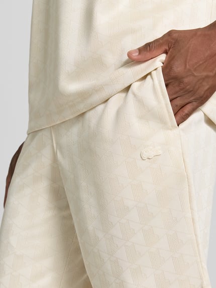 Männermodel trägt Regular Fit Sweatshorts mit Monogramm-Logo-Print von Lacoste in Beige mit feiner Textur, Nahaufnahme Oberkörper, Herren Sweatshorts von Lacoste.