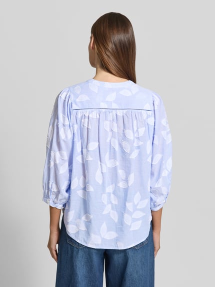 Frauenmodel trägt Regular Fit Bluse mit 3/4-Arm Modell 'FAVIOLA FANCY' von 0039 Italy aus reiner Baumwolle, hinten leicht abgerundet, zartes Hellblau mit weißen Blättermotiven, Ganzkörperansicht Rückansicht.