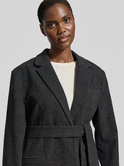 Vrouwenmodel draagt blazer met wol, Materiaalmix, straight fit, reverskraag, knoopsluiting, Model 'Layla' van My Essential Wardrobe, paspelzak op de borst, strookzakken, detailopname bovenlichaam.