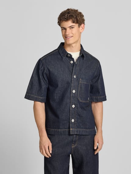 Männermodel trägt Regular Fit Jeanshemd mit Brusttasche von REVIEW aus Reine Baumwolle, dunkles Blau, Kentkragen, Knopfleiste, Ganzkörperansicht von vorne.