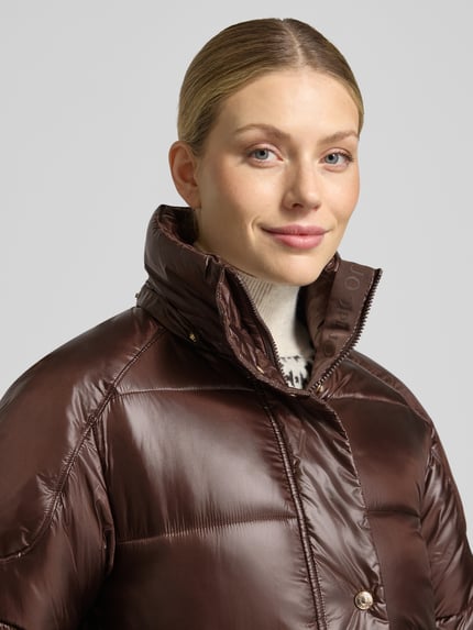 Frauenmodel trägt Steppmantel mit Kapuze von JOOP! in glänzendem Braun, metallische Akzente, Nahaufnahme Oberkörper.