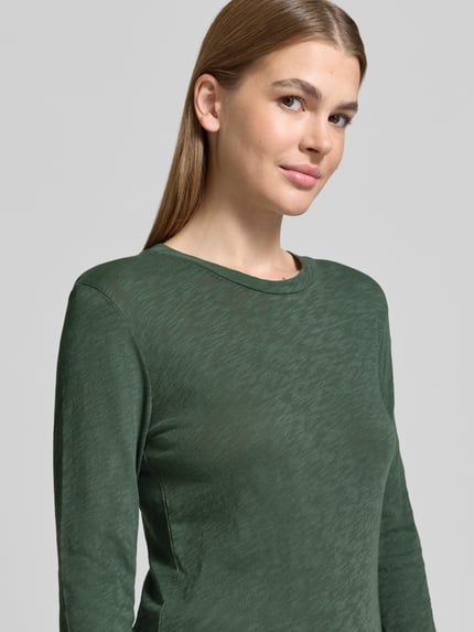 Vrouwenmodel draagt Langarmshirt met abgerond zoom van MARC O'POLO in effen donkergroen, ronde hals, lange mouw, detailopname bovenlichaam.