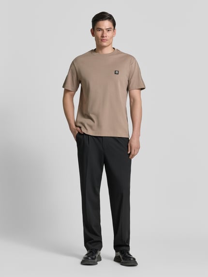Męski model nosi Relaxed Fit T-Shirt aus reiner Baumwolle Modell 'DROSTEE' od HUGO, beżowy jersey, krótki rękaw, naszywka z logo, widok całej sylwetki z przodu.