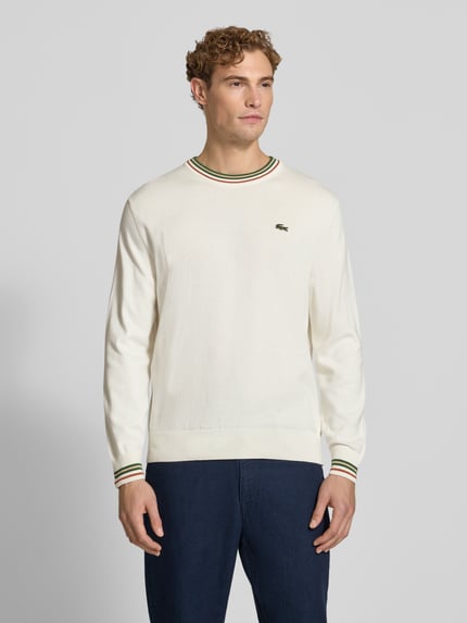 Mannenmodel draagt Regular Fit Pullover aus reiner Wolle van Lacoste in gebroken wit met groene en bruine accenten, Ganzkörperansicht van voren.