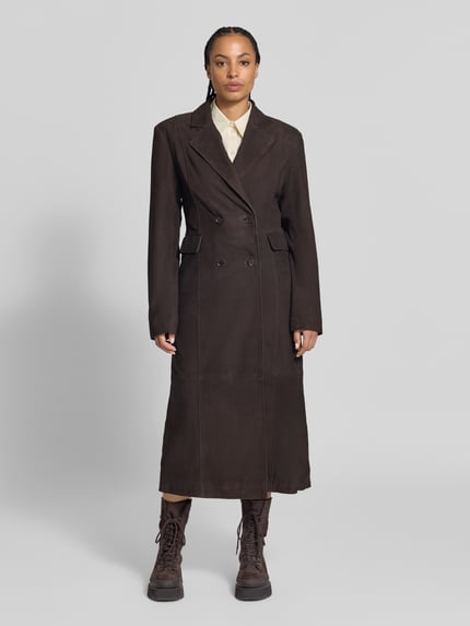 Frauenmodel trägt Ledermantel aus echtem Leder von ROTATE in Dunkelbraun, taillierte Passform, Doppelreiher, Klappentaschen, Ganzkörperansicht von vorne. Rückenlänge 129 cm, Brustweite 42 cm, Ärmellänge 66 cm, Ziegenvelours, Reverskragen.