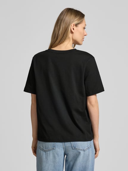 Frauenmodel trägt Relaxed Fit T-Shirt aus reiner Baumwolle von Lacoste in Schwarz, unifarben, Logo-Stitching, Rückansicht Ganzkörperansicht.
