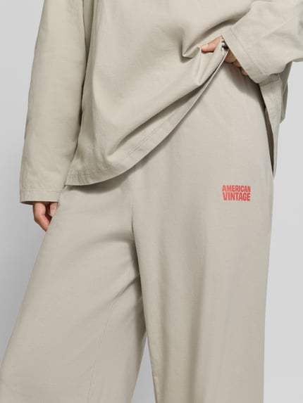 Frauenmodel trägt Wide Fit Hose aus reiner Baumwolle Modell 'GIXY' von American Vintage, beige Farbe, elastischer Bund, Nahaufnahme Oberkörper. Damen Hose aus reiner Baumwolle, Wide Fit, elastischer Bund, Bundweite Größe S 34 cm, Innenbeinlänge Größe S 37 cm.