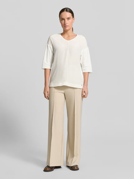 Frauenmodel trägt T-Shirt mit Ärmelaufschlag und Rundhalsausschnitt von Marc Cain aus Baumwoll-Mix mit Stretch-Anteil, Straight Fit, Label-Detail, Rückenlänge bei Größe 36: 62 cm, cremefarbene Textur, Ganzkörperansicht von vorne.
