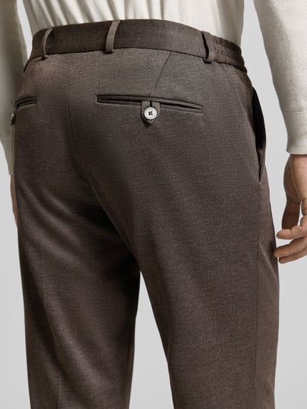 Mężczyzna nosi Anzughose mit Tunnelzug von Zuitable, materiał z domieszką lyocellu, krój slim fit, zaszewki, brązowy kolor, szerokość w rozmiarze 50: 45 cm, długość nogawki wewnętrznej w rozmiarze 50: 85 cm, detaliczne ujęcie tyłu.