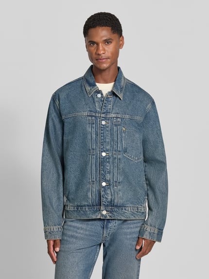 Männermodel trägt Regular Fit Jeansjacke aus Baumwoll-Lyocell-Mix Modell 'AASHTON' von ARMEDANGELS, blaue Denim-Textur, Ganzkörperansicht von vorne. Herren Jeansjacke von ARMEDANGELS.