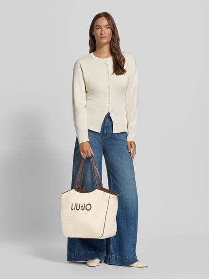 Frauenmodel trägt Shopper aus Teddyfell Modell 'FERIELLE' von Liu Jo White, cremefarbene Struktur, Logo, breite Tragehenkel, Ganzkörperansicht von vorne.