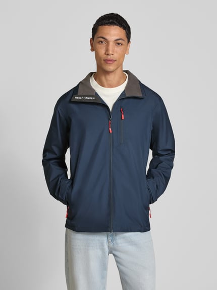 Männermodel trägt Regular Fit Jacke mit Stehkragen Modell 'Crew' von Helly Hansen, dunkelblau mit Logo-Print und Reißverschlusstaschen, Ganzkörperansicht von vorne. Herren Jacke mit Napoleontasche, Eingrifftaschen mit Reißverschluss, Rückenlänge 73 cm, Schulterbreite 48 cm, Brustweite 56 cm, Ärmellänge 68 cm.