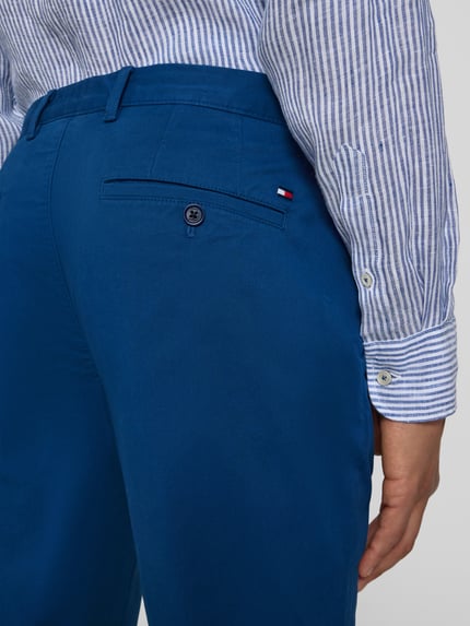 Mężczyznamodel nosi Regular Fit Chino aus Baumwoll-Mix Modell "Denton" von Tommy Hilfiger, efekt: jednolity kolor, mieszanka bawełny, naszywka z logo, szlufki na pasek, zapięcie na guzik i ukryty zamek błyskawiczny, wpuszczane kieszenie, kieszenie z tyłu z guzikiem, detal: guzik, ujęcie: z tyłu, detaliczne zbliżenie na górną część spodni.