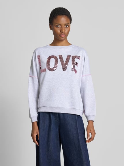 Frauenmodel trägt Oversized Sweatshirt aus reiner Baumwolle Modell 'Love' von miss goodlife, grau mit Statement-Print und Pailletten, Nahaufnahme Oberkörper.