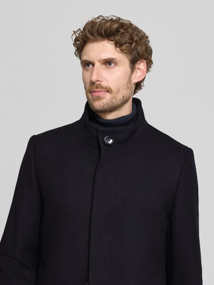 Männermodel trägt Mantel mit Stehkragen Modell 'FINLAN' von STRELLSON in Schwarz, strukturierte Webware, Nahaufnahme Oberkörper.