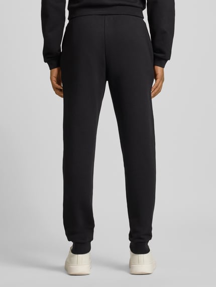 Männermodel trägt Sweatpants mit elastischem Bund und Label-Print von EA7 Armani aus reiner Baumwolle, Regular-Fit, Ganzkörperansicht Rückansicht.