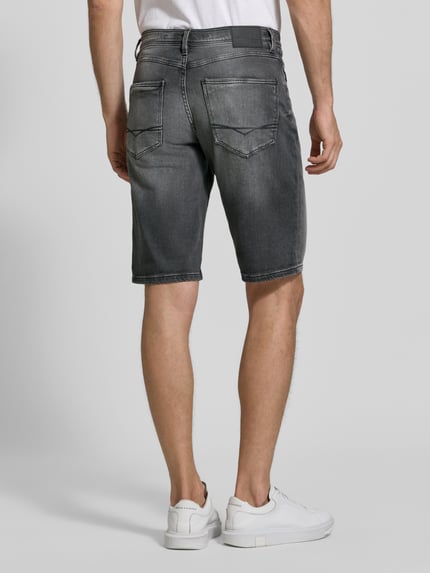 Męski model nosi Bermudas im 5-Pocket-Design mit aufgeschlagenem Saum von Christian Berg Men, Mieszanka bawełny z dodatkiem streczu, krój straight fit, 5 kieszeni, zapięcie na guzik i zamek błyskawiczny, detal z logo, zakładka na dole, Szerokość w rozmiarze 32: 41 cm, Długość wewnętrzna nogawki w rozmiarze 32: 26 cm, szara wyblakła tkanina, tekstura jeansu, Ganzkörperansicht Rückansicht.