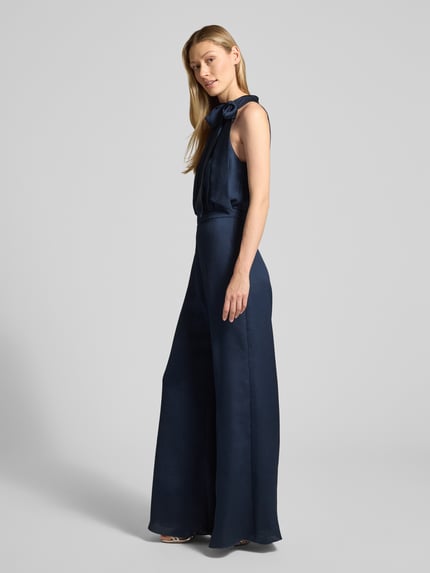 Frauenmodel trägt Jumpsuit mit Schleifen-Detail von Swing in Dunkelblau, Regular Fit, Neckholder, weich fließende Stoffstruktur, Ganzkörperansicht von vorne.
