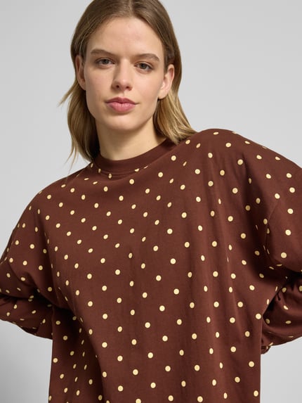 Kobiece modelka nosi Sweatshirt mit überschnittenen Schultern od OH APRIL, luźny krój, okrągły dekolt, elastyczne zakończenia rękawów, długość tyłu w rozmiarze S: 69 cm, brązowa bluza w jasne kropki, zbliżenie na górną część ciała