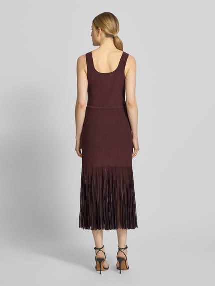 Frauenmodel trägt Strickkleid aus Rippstrick von BOSS in dunklem Rot, knielang, ohne Ärmel, Transparente Plisseefalten, Ganzkörperansicht Rückansicht.