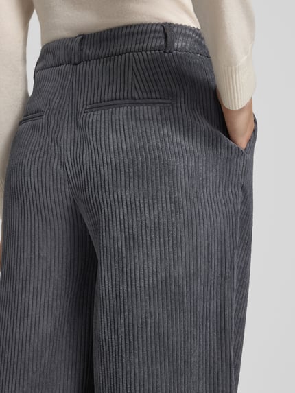 Vrouwenmodel draagt Wide Leg bandplooibroek uit corduroy van comma, antraciet met paspelzakken achter, bandwijdte maat 36/32: 35 cm, binnenbeenlengte maat 36/32: 78 cm, detailopname rugzijde.