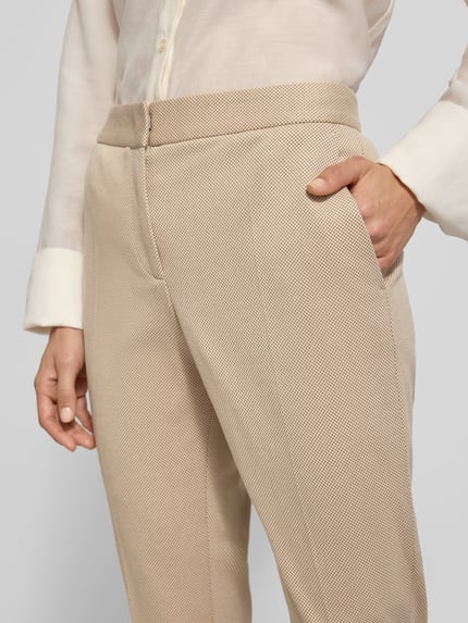 Kobiece modelka nosi Regular Fit schmale Hose aus Viskose-Mix Model 'Tapria-Crop4' od BOSS w beżowym kolorze z fakturą, wzór allover, detaliczna kieszeń, zapięcie na guzik, schiebehaken i zamek, boczne kieszenie, materiał viskoza-mix, detaliczna tekstura, zbliżenie na górną część ciała.