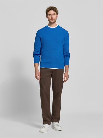 Männermodel trägt Regular Fit Strickpullover aus Baumwoll-Mix von MCNEAL in Blau, braune Hose, weiße Sneaker, Ganzkörperansicht von vorne. Herren Strickpullover, Rundhalsausschnitt, elastische Abschlüsse, Rückenlänge 65 cm, Ärmellänge 56 cm.