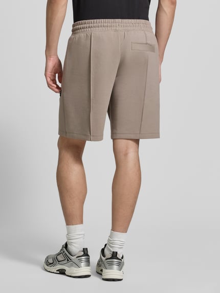 Mannelijk model draagt Regular Fit Sweatshorts uit katoenmix model 'DIMACSHORT' van HUGO, look: effen, regular fit, labelpatch, elastische boord met tunnelkoord, zij-steekzakken, materiaalverwerking: sweat, kleur is beige, mix van katoen, ganzlichaams aanzicht achterkant.