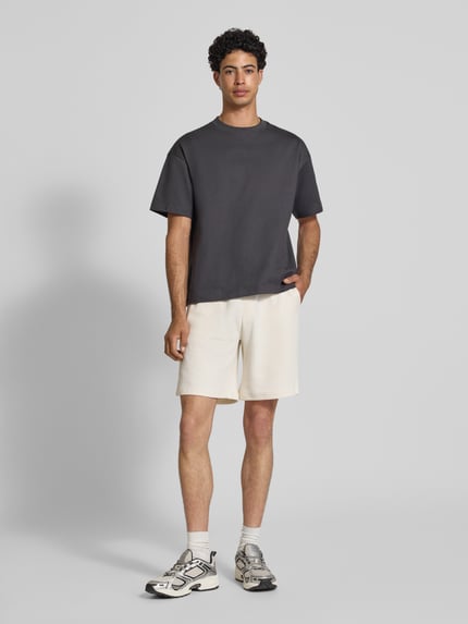Männermodel trägt Shorts aus Baumwoll-Mix mit Strukturmuster Modell 'KNOX' von Redefined Rebel in Naturweiß mit elastischem Bund, Relaxed Fit, Ganzkörperansicht von vorne.