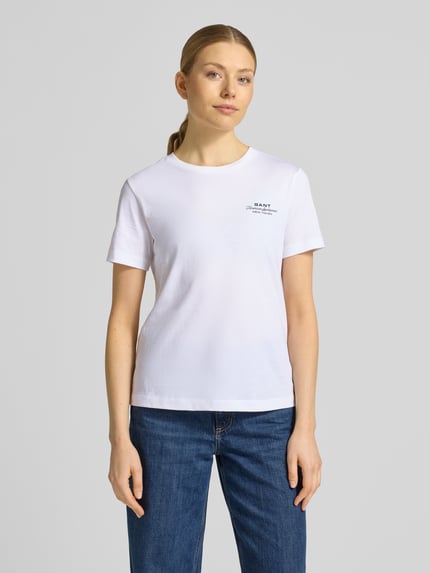 Frauenmodel trägt T-Shirt mit Label-Print und Rundhalsausschnitt von Gant, Damen T-Shirt aus Reine Baumwolle, Regular-Fit, Weiß, Rückenlänge bei Größe S: 57 cm, Ganzkörperansicht von vorne.
