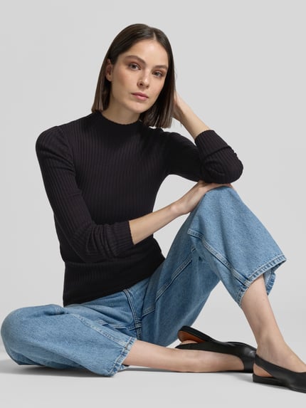 Vrouwenmodel draagt gebreide pullover uit puur katoen model 'ALAANIA' van Armedangels, look: effen, slim fit, labelpatch, logostitching, mock neck, hooggesloten hals, lange mouw, materiaalverwerking: knitwear, kleur: zwart, voorkantperspectief, halve lichaamsopname.